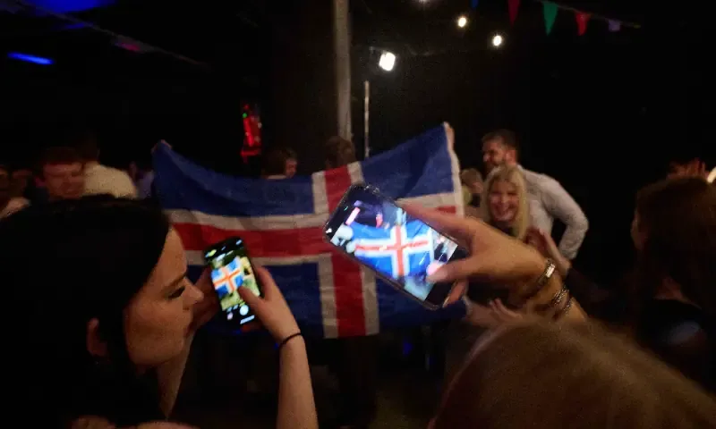 Women take pictures with their mobile phones as supporters wave an Icelandic flag during a referendum night event organised by Sfram Island, the “No” campaign against resuming Iceland's European Union accession negotiations, in Reykjavik, Iceland, on Aug 30, 2026. — AFP